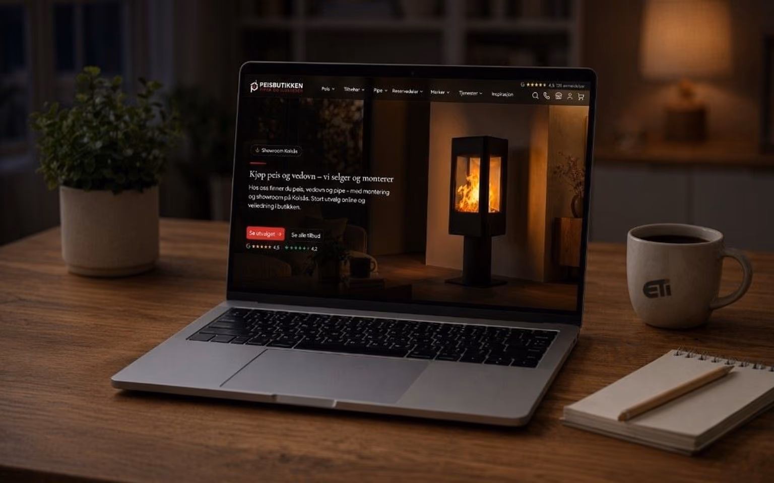 Laptop på lyst trebord som viser Peisbutikken-forsiden, med eti-logo på kaffekoppen
