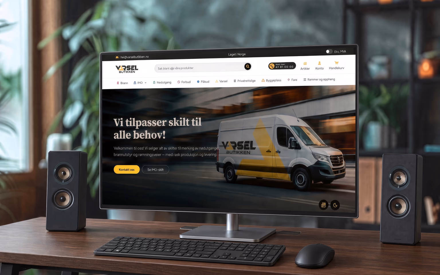 Skjerm på trebord som viser Varselbutikken-forsiden, med høyttalere og planter